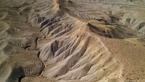 A-spectacular-4K-drone-shot-over-the-barren,-desert-hills-of-Grand-Valley-OHV-area,-with-the-steep-sloped-plateaus-of-the-Little-Book-Cliffs-in-the-distance,-located-in-Grand-Junction,-Colorado