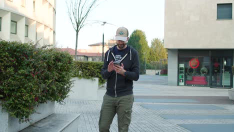 Casual-young-man-standing-in-urban-area-scrolling-and-tapping-smartphone
