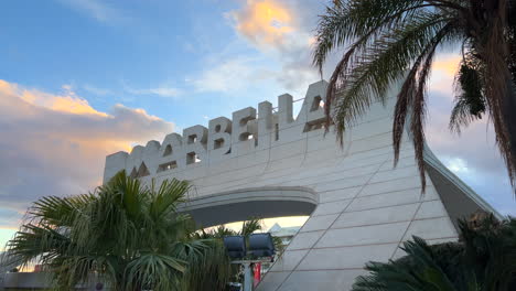 Gran-Cartel-De-Marbella-Con-Nubes-Naranjas-Al-Atardecer-En-España,-Bonito-Cielo-Y-Palmeras,-Toma-De-4k