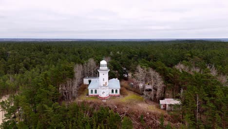 lighthouse-standing-tall-amidst-a-dense-forest,-the-edge-of-the-ocean-is-not-visible,-Aerial-Orbit-Pan-Shot