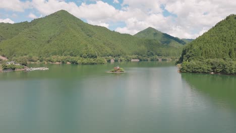 Panoramic-mountain-range-landscape-in-pristine-turquoise-japanese-lake-temple-shinto-religious-shrine-build-in-the-middle-of-the-water,-summer-in-japan,-morning-skyline