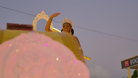 Beauty-pageant-winner-dances-blowing-kisses-across-onlookers-as-she-stands-on-top-of-golden-float