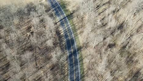 Drone-Aerial-view-of-a-red-car-driving-on-a-road-surrounded-by-woods-in-early-spring-in-Pataskala-Ohio