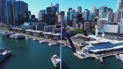 Drone-Giratorio-Aéreo-Que-Establece-Un-Arco-De-Australia-Darling-Harbour-En-Sydney-Con-La-Bandera-Australiana-En-El-Centro-Y-El-Horizonte-De-La-Ciudad-Al-Fondo