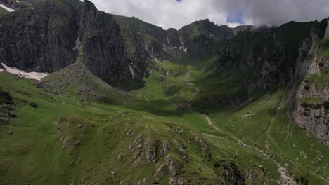 Lush-green-valley-nestled-between-Bucegi-Mountain-peaks,-with-a-clear-blue-sky-and-rugged-terrain