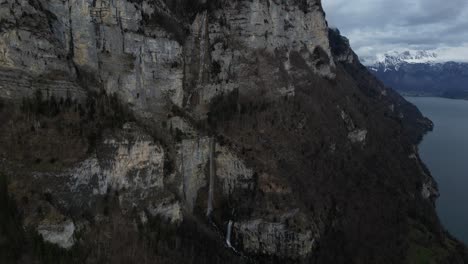 Vista-De-Drones-De-Un-Acantilado-De-Una-Colina-Con-Montañas-Al-Fondo-En-Walensee,-Suiza