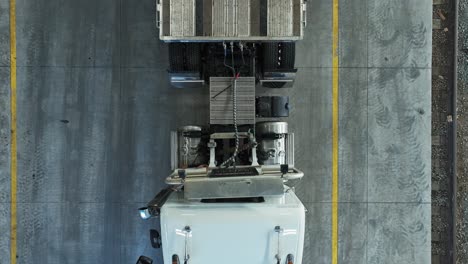 Drone-top-down-tracking-pan-across-semi-truck-and-empty-trailer-in-warehouse