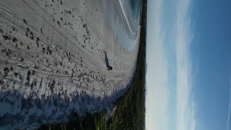 Vertical-drone-shot-of-driving-car-on-sandy-beach-along-coastline-of-Australien-coast