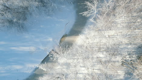 Low-winter-sun-casting-long-horizontal-shadow-lines-on-beautiful-frozen-river-and-snow-landscape-in-Finland,-Top-Down-Aerial