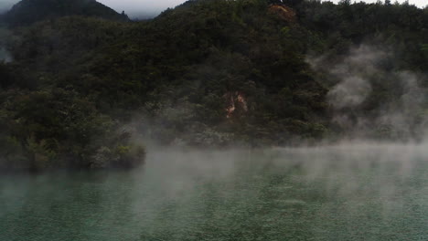 Slow-fly-over-steaming-geothermal-pond-in-volcanic-region-of-New-Zealand,-North-Island