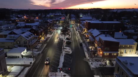 Twilight-over-a-snowy-main-street-in-a-small-town-with-cars-and-lit-storefronts