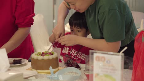 Kind-Voller-Freude-Und-Aufregung-Schneidet-Einen-Kuchen-Am-Geburtstag,-Von-Erwachsenen-Geführt