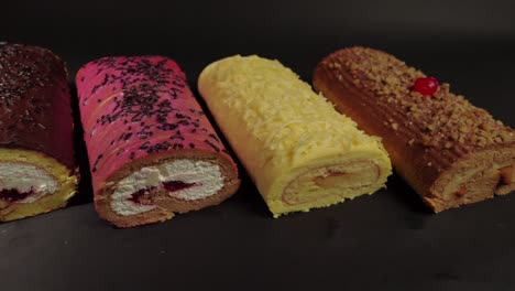 top-view-flat-shot-of-slider-shot-of-cake-rolls-brazo-gitano-swiss-roll-desserts-collection-chocolate-ferrero-cheese-butter-jelly-berries-cherry-with-black-background