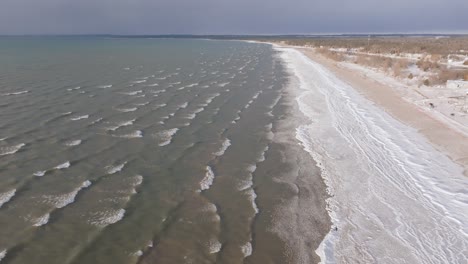 Ein-Ruhiger-Sandstrand-Mit-Sanften-Wellen-Und-Klarem-Himmel,-Die-Küste-Erstreckt-Sich-In-Die-Ferne,-Luftaufnahme