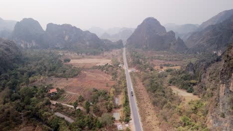 Carretera-De-Suministro-Atravesando-Un-Paisaje-Kárstico-árido-Y-Lleno-De-Niebla-Tóxica-Durante-La-Estación-Seca-Del-Norte-De-Laos
