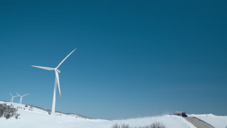 Daegwallyeong-Sky-Ranch---Massive-Wind-Turbines-Rotate-Blades-Against-Blue-Sky-as-Tractor-with-Trailer-Bring-People-to-Mountain-Summit,-South-Korea-Travel