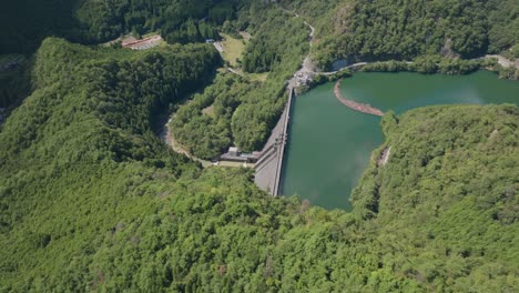 Luftdrohne-Fliegt-über-Dem-Damm-In-Der-Blauen-Wasserlandschaft-Von-Kyoto,-Ruhiger-Flussfluss-Im-Zen-grünen-Zedernwald,-Japanische-Naturumgebung-Im-Kansai-Tageslicht