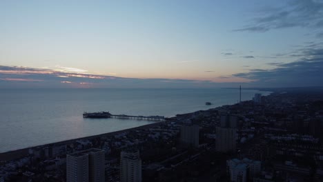 Paisaje-Aéreo-De-Drones-Al-Atardecer-En-Brighton-East-Sussex,-Inglaterra,-Horizonte-Azul-Del-Mar,-Gradiente-De-Magenta,-Incendios-En-Un-Ambiente-Tranquilo