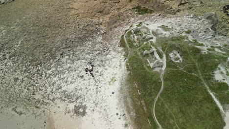 Downward-Arc-Aerial-View-of-a-Ruined-Building-Next-to-Sandy-Beach-and-Ocean