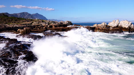 Drone-pullback-shot-of-ocean-waves-smashing-into-Hermanus-rocky-coastline