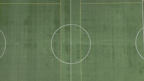 The-drone-records-an-upward-shot-of-the-football-stadium,-commencing-with-the-center-circle-and-concluding-with-the-entire-pitch-occupying-the-frame