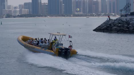 Tourists-in-Speedboat-Sailing-In-Front-of-Abu-Dhabi-Cityscape-Skyline-and-Waterfront-Buildings,-The-Yellow-Boats-Cruise-Company