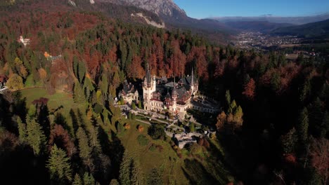 Peles-castle-with-autumn-colored-trees-at-sunset,-showcasing-historic-architecture,-aerial-view