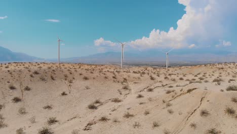 Slow-fly-up-and-over-of-sand-covered-hills-and-windmills-near-small-desert-town