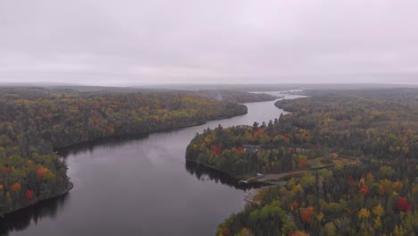 Drone-shot-flying-over-a-gorgeous-river-surrounded-by-trees-changing-color-in-the-fall-time