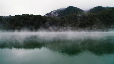 Fly-through-stream-hovering-over-surface-of-volcanic-lake-towards-lush-forest-in-New-Zealand