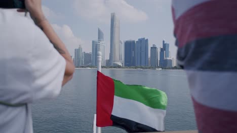 Abu-Dhabi-UAE-Cityscape-Skyline-and-Etihad-Towers,-Tourists-and-National-Flag-on-Cruise-Ship