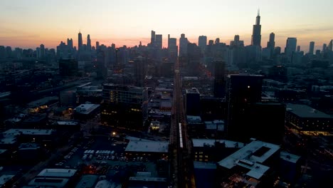 A-captivating-drone-aerial-view-of-a-Chicago-at-dusk,-showcasing-illuminated-skyscrapers-against-the-darkening-sky-The-golden-hues-of-sunset-paint-a-serene-backdrop,-highlighting-architectural-marvels