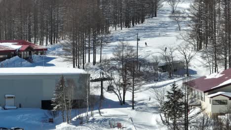 Einspielung-Des-Fußes-Der-Skipisten,-Skifahrer-Kommen-Am-Fuße-Des-Berges-An,-Wo-Die-Gondeln-Der-Seilbahn-Aus-Der-Umlaufbahn-Abfahren,-Teleskopaufnahme-Einer-Japanischen-Skipiste,-Region-Hakuba-Und-Myoko