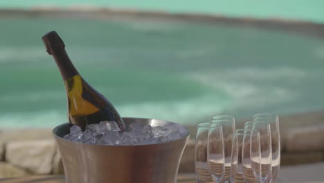 Ein-Kellner-Bringt-Eine-Flasche-Champagner-Auf-Eis-Zu-Einem-Tisch-Am-Pool-In-Einem-Luxusresort