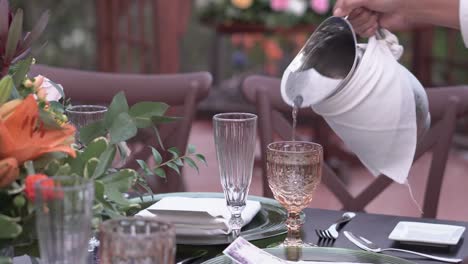 Waiter-pours-water-into-glass-glass-during-outdoor-wedding-reception