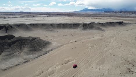 Tracking-Drone-Shot-of-Red-SUV-Vehicle-Moving-on-Dry-Barren-Lifeless-Desert,-Utah-USA