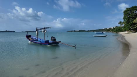 Ruhiger-Thailändischer-Strand-Mit-Booten-An-Klaren-Tagen,-Goldener-Sand,-Der-In-üppiges-Grün-übergeht,-Heitere-Meereslandschaft