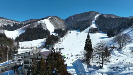 Low-angle-drone-shot-of-bottom-of-ski-run,-skiers-arriving-at-base-of-mountain-lining-up-for-the-chairlifts