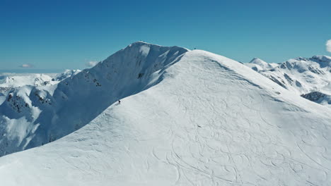 Snow-covered-mountain-peak-under-clear-blue-sky-with-ski-tracks,-vast-alpine-winter-landscape