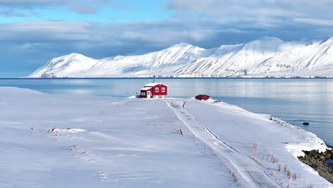 Hermoso-Paisaje-De-Una-Sola-Casa-Roja-Al-Borde-De-Un-Fiordo,-Rodeada-De-Nieve-Y-Montañas