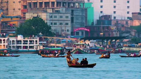 Barqueros-Remando-En-El-Bullicioso-Río-Buriganga-Con-El-Paisaje-Urbano-De-Dhaka-Y-Otros-Barcos-En-El-Fondo,-Colores-Vibrantes