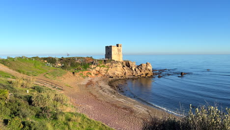 Torre-de-la-Sal-in-Casares-Manilva-beach-in-Spain,-coastal-tower-system-for-surveillance-and-defence-against-Berber-pirates,-green-plants-at-the-sunny-beach,-4K-shot