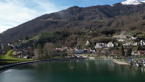 Drohnenclip-Mit-Blick-Auf-Traditionelle-Weiße-Gebäude-Am-Ufer-Eines-Ruhigen-Sees-Mit-Schneebedeckten-Bergen-Im-Hintergrund