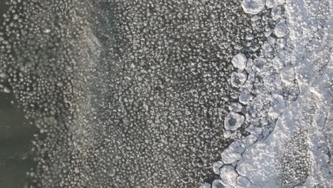 A-frozen-lake-with-intricate-ice-patterns-and-clear-water-at-the-edge,-aerial-view