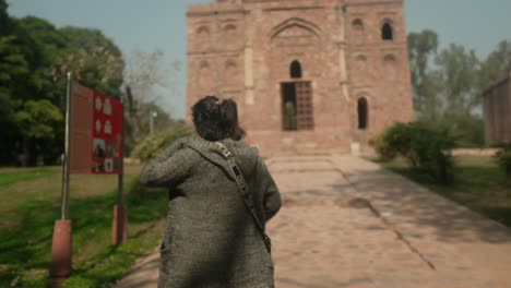 Mujer-Acercándose-A-Un-Antiguo-Templo-De-Ladrillo-En-Un-Día-Soleado,-Con-La-Mochila-A-Cuestas,-Explorando-El-Patrimonio-Cultural