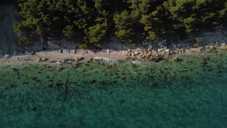 Tilt-down-aerial-shot-of-a-beach-near-forest-in-Split,-Croatia,-during-summer