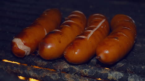Close-up:-Sausages-split-as-they-cook-on-open-campfire-grill-at-night
