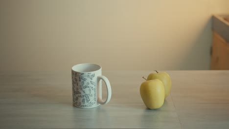 Static-Shot-Of-A-Cup-Of-Coffee-And-Two-Green-Apples-On-Kitchen-Table