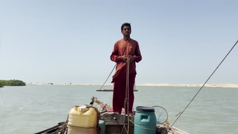 Fisherman-in-red-clothes-stands,-on-a-boat-on-the-River-Indus
