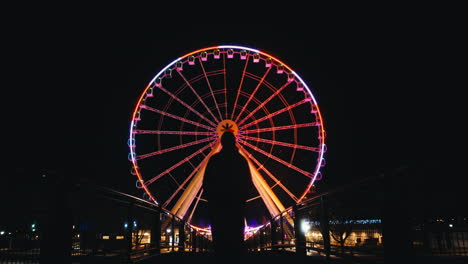 Silhouette-of-Person-Waking-Towards-Colorful-Ferris-Wheel,-Nighttime